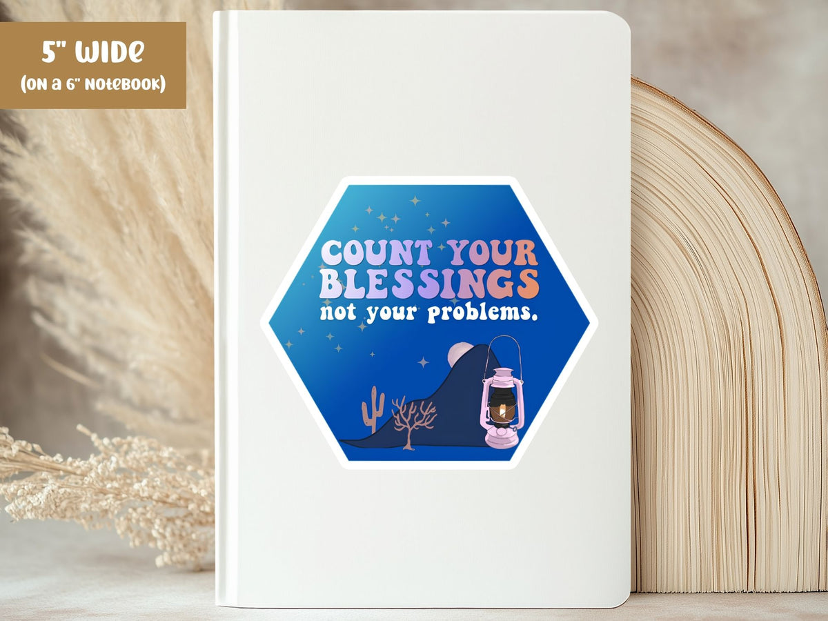 "Count Your Blessings, Not Your Problems" blessing sticker, 5-inch size, on the cover of a white 6-inch notebook