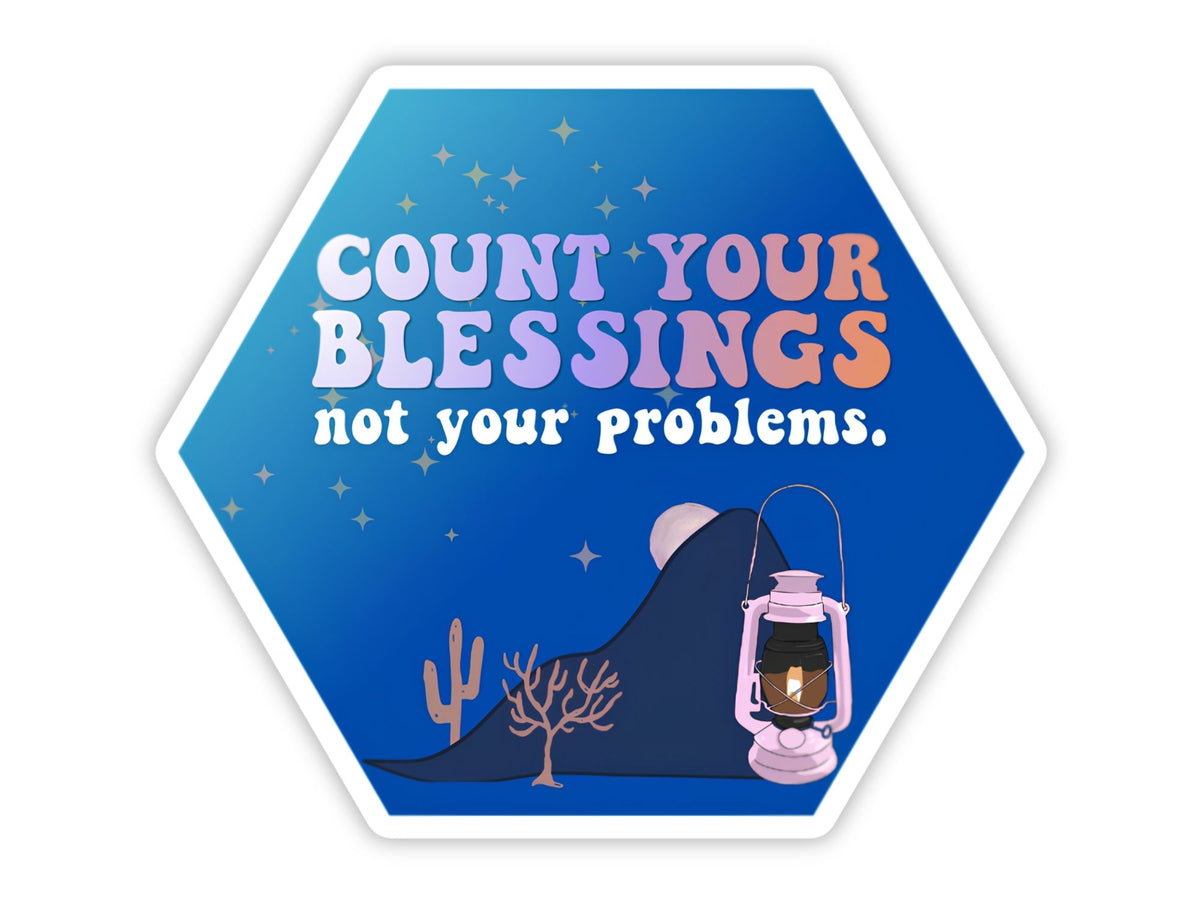 "Count Your Blessings, Not Your Problems" blessing sticker. A hexagon night sky with stars, a glowing pink lantern against dark mountains, a cactus, and a bare tree