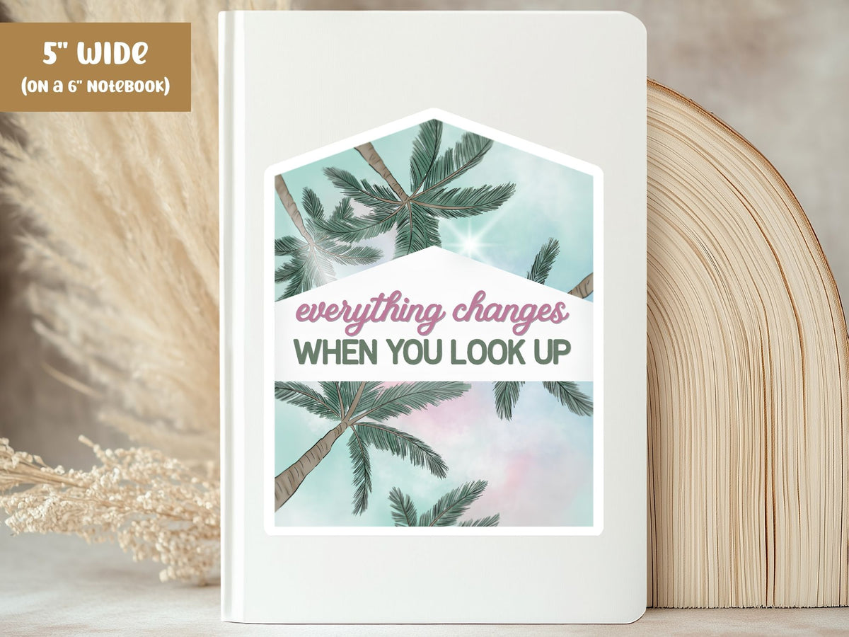"Everything Changes When You Look Up" palm tree sticker, 5-inch size, on the cover of a white 6-inch notebook