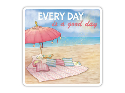 "Every Day is a Good Day" beach positivity sticker. A pink fringed umbrella over a striped beach blanket piled with pillows, with sparkling turquoise water and a bright sun