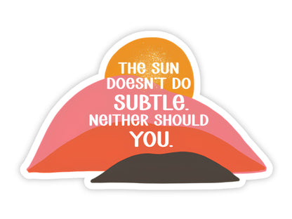 "The Sun Doesn't Do Subtle. Neither Should You." confidence sticker. A bold orange sun rising over layered pink, coral, and dark brown desert hills